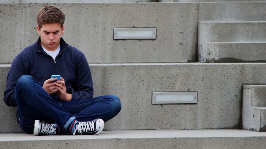 Frustrated teenage boy staring at his phone, representing teen anger issues and parents attempting to understand it.